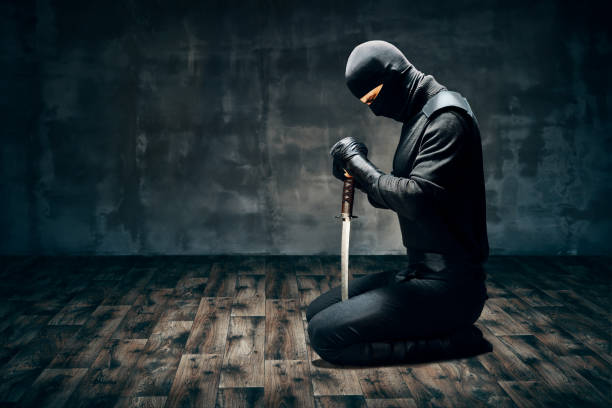 Warrior man sitting on floor posing with a sword Warrior man sitting on floor posing with a sword over dark background harakiri photos stock pictures, royalty-free photos & images