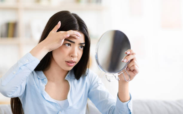 istock Problem Skin. Worry Asian Woman Looking In Round Mirror And Touching Forehead 1270411132