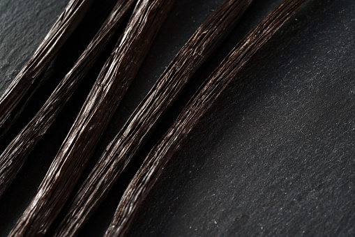 Five bourbon vanilla beans on black slate desk, closeup view from above