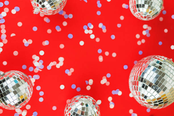 Disco mirror ball Christmas tree toy on a bright festive red background with scattered confetti. Christmas and New Year holiday concept. View from above. Flat lay. stock photo