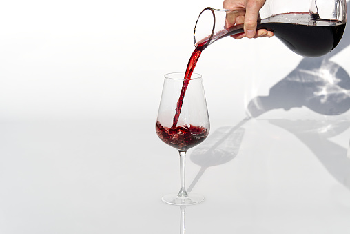 Sommelier pours red wine from decanter to wineglass on white background