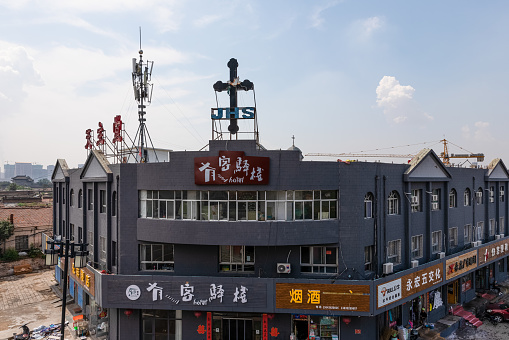 Datong, China - August 19, 2020:  Parish catholic church with big cross enclosed and shaded by commercial buildings with shops and restaurants in Datong Old City under rebuilding, Shanxi, China.
