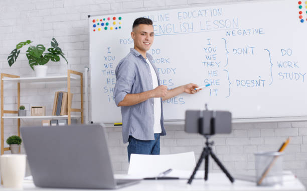 istock Online tutor remote. Smiling young man points to whiteboard, looks at webcam 1270413097