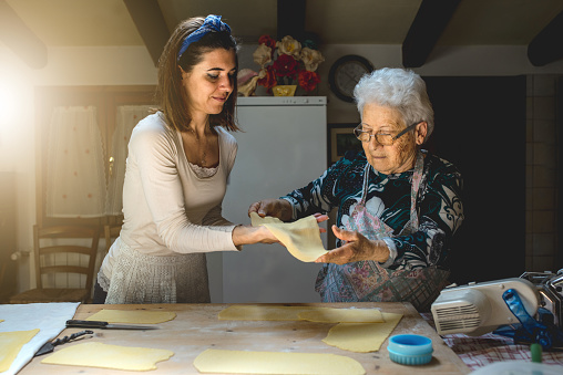 Retrato nieta y abuela preparando pasta casera fresca en la cocina. Tradiciones familiares. photo