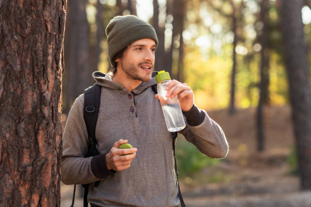 bel ragazzo che beve acqua mentre cammina nella foresta - drinking men water bottle foto e immagini stock