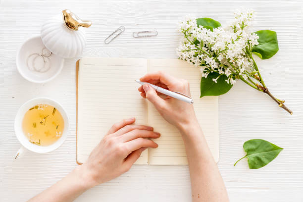 istock Female hands writing on notebook. Workplace with flowers bouquet top view 1270415471