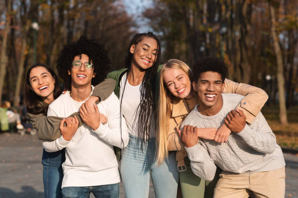 Positive group of young friends having fun at public park Positive group of multiracial young friends having fun at public park, hugging and smiling friends laughing stock pictures, royalty-free photos & images