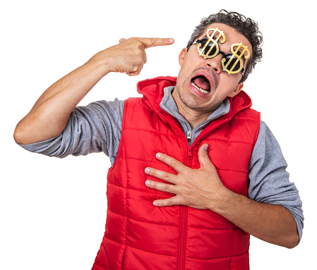 Man in a red vest making a gun gesture with his hand pointing to his forehead with an agonized expression. The man is wearing golden dollar shaped sunglasses. Isolated on white.