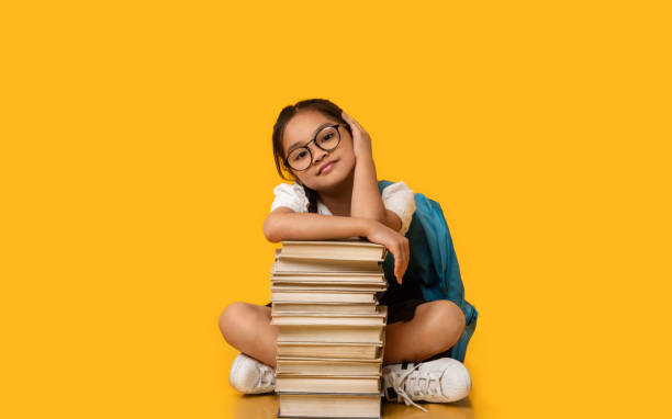 istock Korean Schoolgirl Sitting At Books Stack In Studio, Yellow Background 1270415881