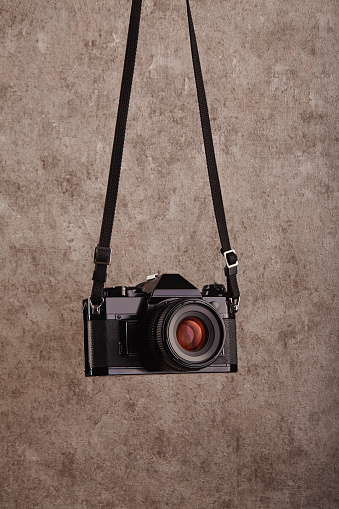 Old-fashioned professional vintage SLR analog film camera hanging in front of a concrete textured wall as background