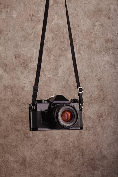 Old-fashioned professional vintage SLR analog film camera hanging in front of a concrete textured wall as background Old-fashioned professional vintage SLR analog film camera hanging in front of a concrete textured wall as background strap photos stock pictures, royalty-free photos & images