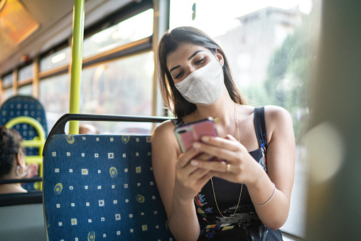 Young woman wearing face mask using phone on the bus