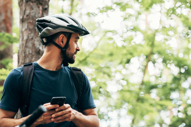 istock Horizontal outdoor image of cyclist man resting in the forest, holding smartphone, using online application for searching GPS coordinates while riding a bike. Travel, sport, modern technology concept 1270418573