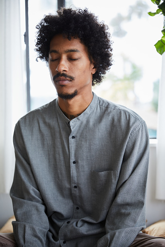 Young African American man sitting with his eyes closed on his bed during a meditation session