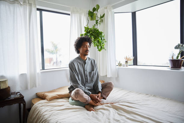 istock Young man sitting on his bed with his eyes closed and meditating 1270419863