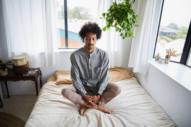 jeune homme s’asseyant les jambes croisées sur son bâti et méditant - men yoga meditating cross legged photos et images de collection