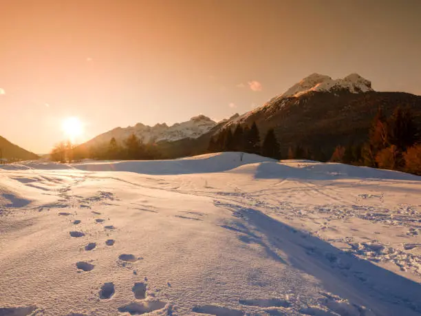 Footprints in the fresh snow with a view of the snow capped Italian Alps of the Brenta Dolomites in a late afternoon at sunset.