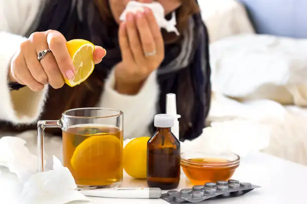 a young unrecognaseble woman with a cold or flu laying on the bed and preparing tea with lemon. Alternative medicine, home treatments and seasolan illnesses concept