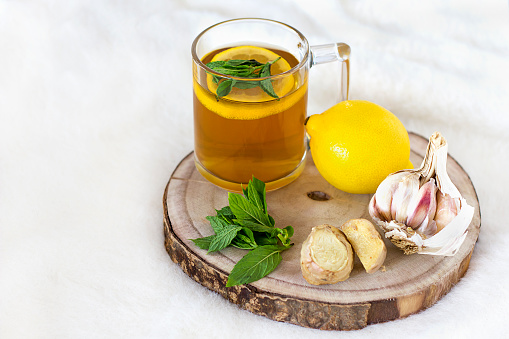 alternative remedies for colds and flu. home treatment. Transparent cup of herbal tea, mint, lemon, garlic, ginger and honey on a wooden tray on a light background. Space for text