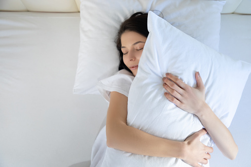 Woman sleeping in bed hugging white pillow