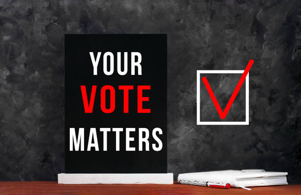 istock Your Vote Matters text sign on black chalkboard with white notebok and red pen on dark background. Make a political choice. 1270428067