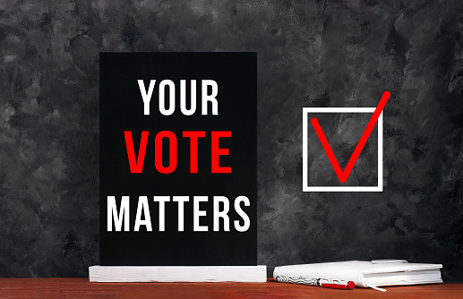 Your Vote Matters text sign on black chalkboard with white notebok and red pen on dark background. Message written on blackboard display. Vote elections concept. Make the political choice.