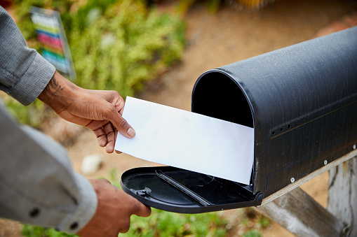 Closeup of a young African American man standing outside of his house and taking a letter out of his mailbox