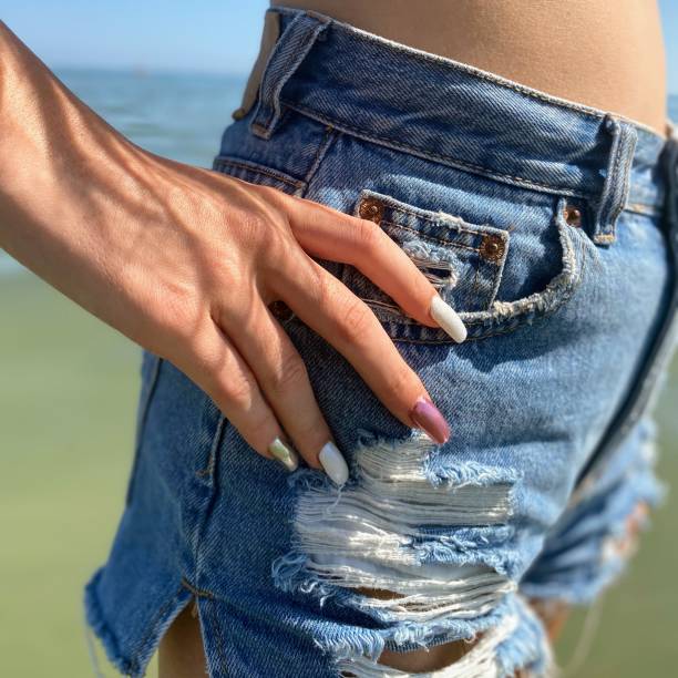 giovane ragazza con le mani curate appoggiate su pantaloncini in denim strappati - denim shorts foto e immagini stock