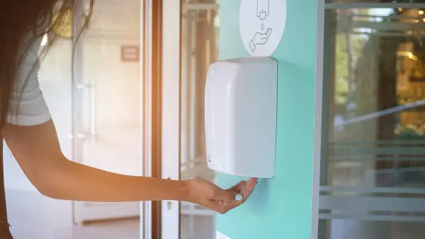 female hand with antibacterial gel from automatic sanitize machine hanging on building wall healthcare concept outdoor