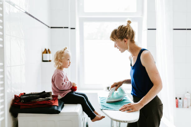 子供を持つ若い母親がトイレでタオルをアイロンをかけて - iron laundry cleaning ironing board ストックフォトと画像