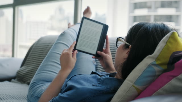 Young Woman Relaxing Reading Ebook On Sofa At Home