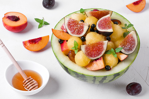 Fruit salad with yellow watermelon, fig, nectarine, plum, bilberry, apple, banana and honey in the watermelon half