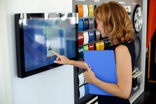 Female saleswoman in a car dealership. About 40 years old, Caucasian blonde redhead.