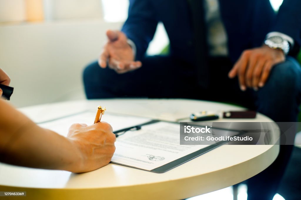 Signing a contract Salesman and a customer in a car dealership. Mixed race male and a blonde female. Car Insurance Stock Photo