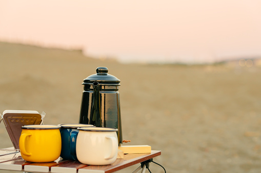 Coffee mugs and a coffee pot at the beach.