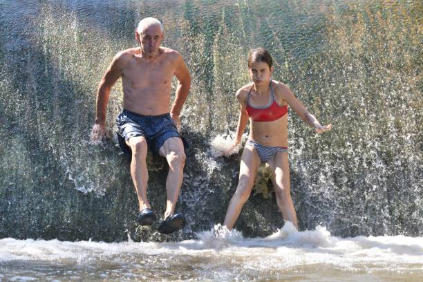 PORTRAIT, CLOSE UP: Happy Caucasian girl splashing refreshing water while swimming in the pond being filled by the crystal clear forest stream. Cheerful woman splashing and outstretching her arms.