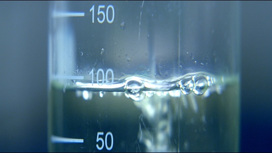 Professional scientific beaker tub glass with metric scale filling with transparent liquid of water viscosity. full frame macro close up vaccine research concept shot with selective focus.