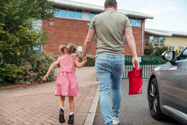 Back To School Close-up of a caucasian father walking his little girl into the school gates ready for her first day back. northern europe family car stock pictures, royalty-free photos & images