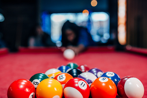 Close-up of a player's hand guiding the cue stick with focused precision to hit a billiard ball on a blue pool table.