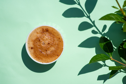 Cup of coffee on green background with strong shaddow top view
