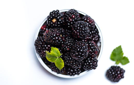 Fresh blackberry fruit in a bowl with leaves on white background isolated. Healthy and natural sweet food