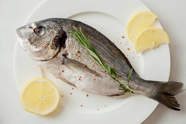 istock Raw dorado with lemon, pepper and rosemary on a plate, top view. 1270471237