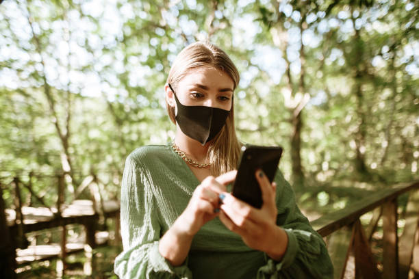 istock Young woman with protective face mask using her smart phone in a forest 1270475118