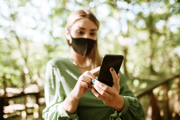 istock Young woman with protective face mask using her smart phone in a forest 1270475171