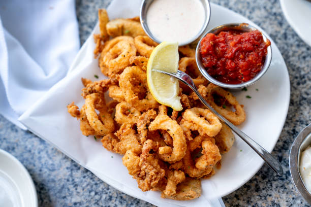 une délicieuse assiette de calamars frits, calmar frit à la perfection style cajun, servi avec un côté de sauce aioli à l’ail fraîchement fait et sauce cocktail, quartiers de citron frais sur le côté - fry up photos et images de collection