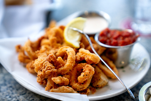 A Delicious Plate Of Deep Fried Calamari, Squid Fried To Perfection, Cajun Style Served With A Side Of Freshly Made Garlic Aioli Sauce And Cocktail Sauce, Fresh Lemon Wedges On The Side