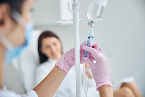 enfermera calificada añadiendo un medicamento a un frasco de perfusión - alternative therapy fotografías e imágenes de stock