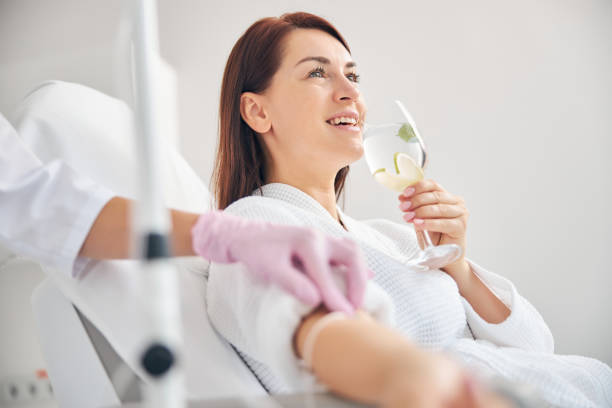 atractiva mujer de pelo oscuro sonriendo durante la terapia intravenosa - vitamina fotografías e imágenes de stock