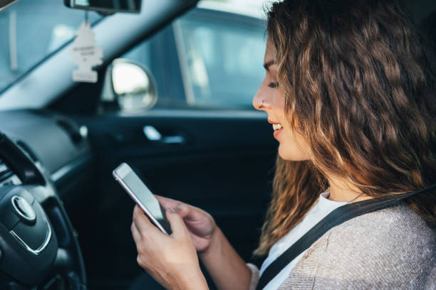молодая женщина, используя смартфон в автомобиле фондовых фото - mobile phone seat belt text messaging smiling стоковые фото и изображения