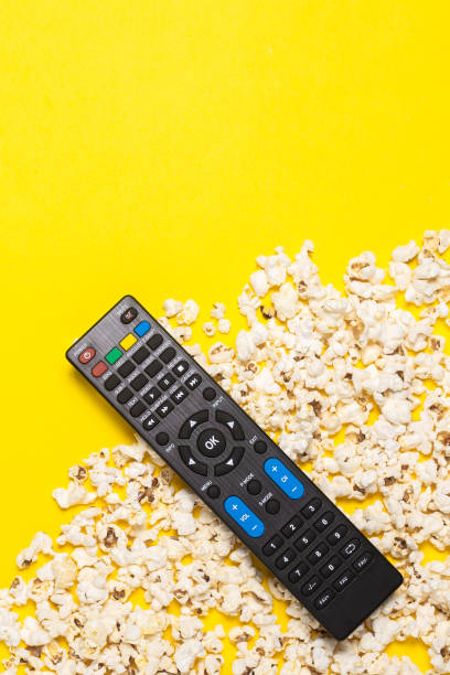 istock TV remote control, TV tuner or audio system and popcorn on a yellow background. Concept series, film, sports. Banner. Flat lay, top view 1270498975